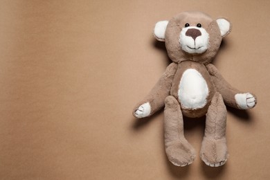 Cute teddy bear on brown background, top view. Space for text