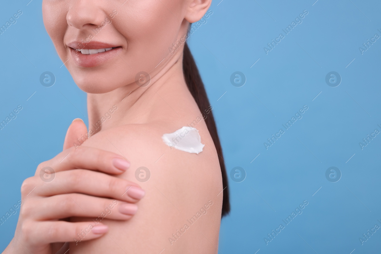 Photo of Woman with smear of body cream on her shoulder against light blue background, closeup. Space for text