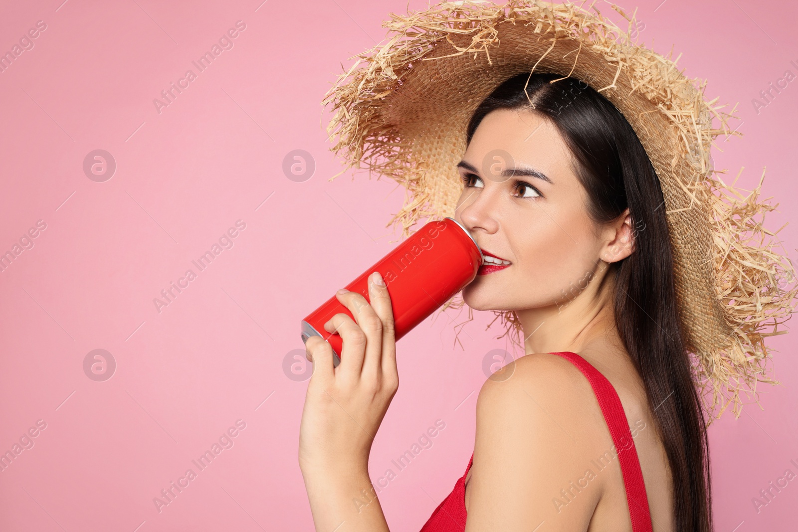 Photo of Beautiful young woman with straw hat drinking from tin can on pink background. Space for text