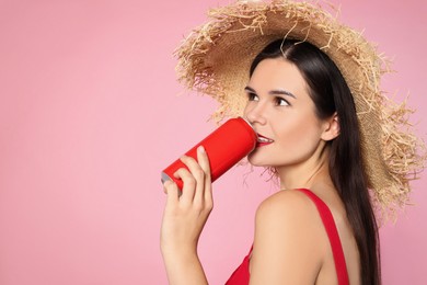 Photo of Beautiful young woman with straw hat drinking from tin can on pink background. Space for text
