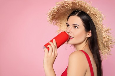 Beautiful young woman with straw hat drinking from tin can on pink background. Space for text