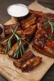 Photo of Tasty roasted pork ribs served with rosemary on wooden table, closeup
