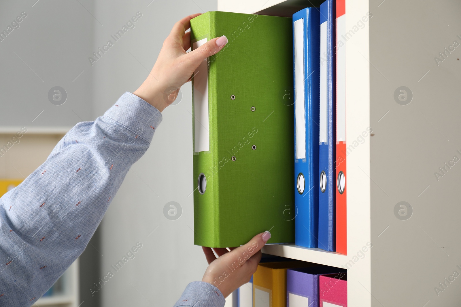 Photo of Woman taking binder office folder from shelving unit indoors, closeup