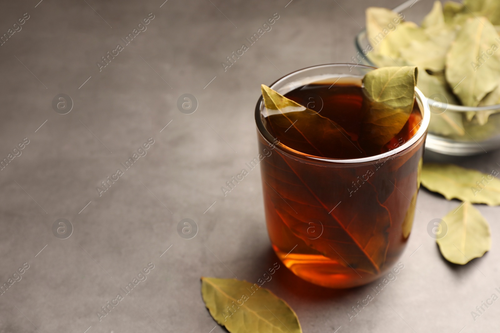 Photo of Cup of freshly brewed tea with bay leaves on grey table. Space for text