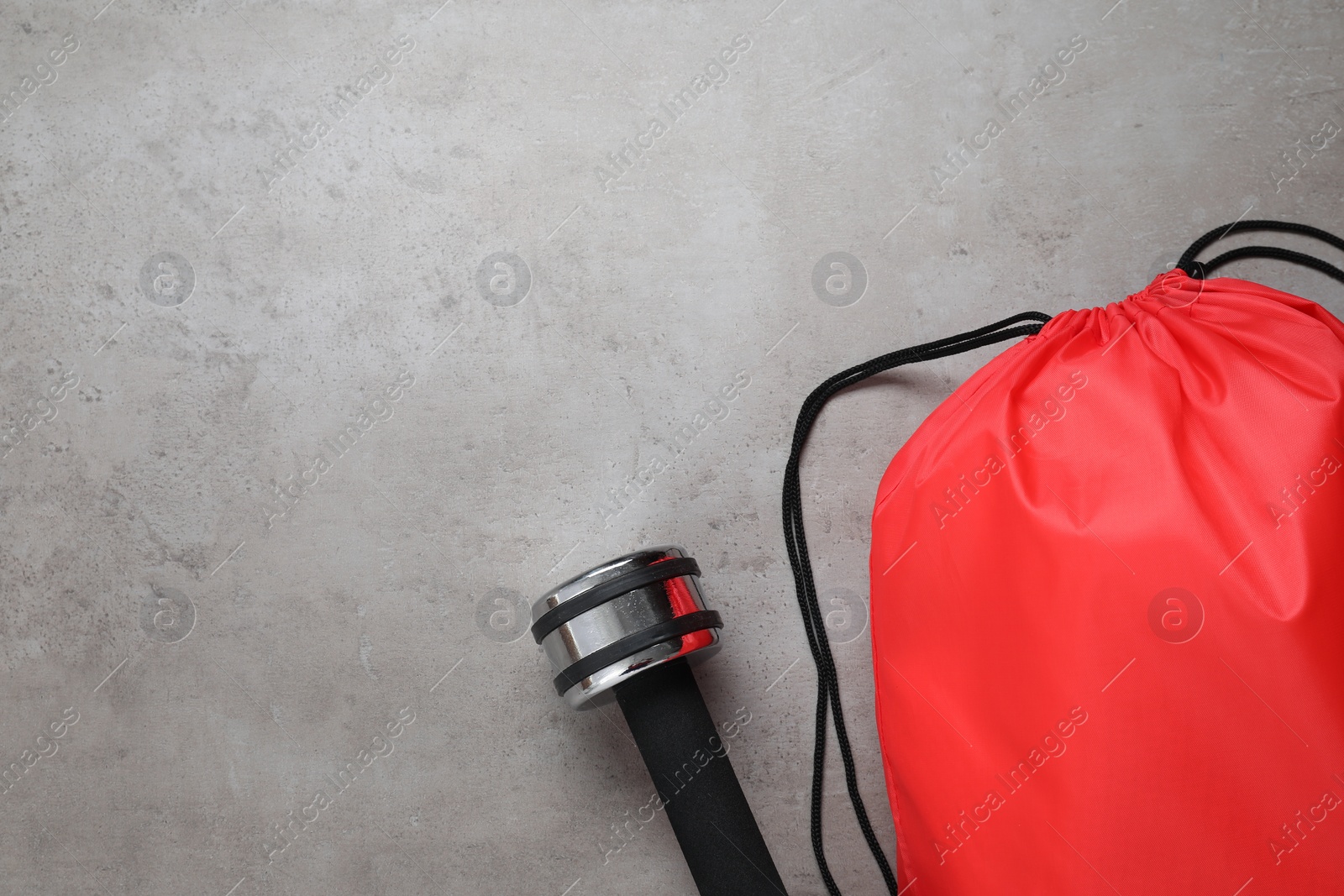 Photo of Red drawstring bag and dumbbell on grey textured background, flat lay. Space for text