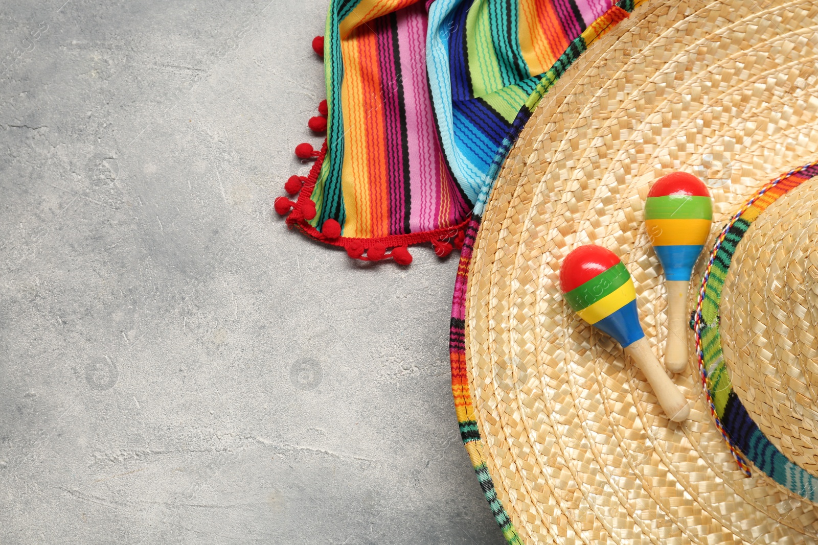 Photo of Mexican sombrero hat, maracas and colorful poncho on grey textured background, flat lay. Space for text