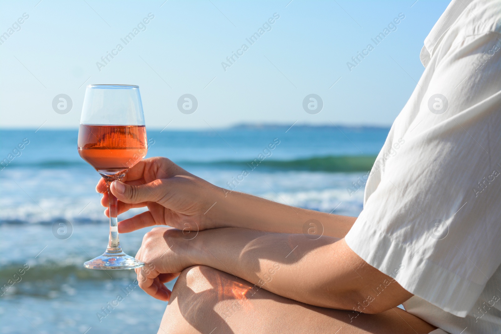 Photo of Woman with glass of tasty rose wine near sea, closeup