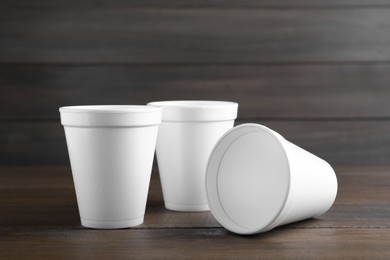 Photo of Three white styrofoam cups on wooden table