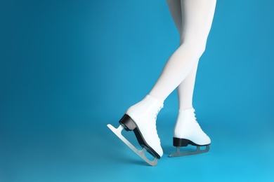 Woman in elegant white ice skates on light blue background, closeup of legs. Space for text