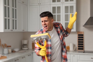 Photo of Man with mop singing while cleaning at home