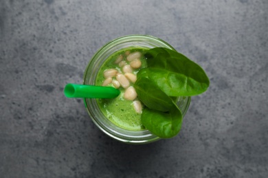 Jar of healthy green smoothie with fresh spinach on grey table, top view