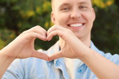 Man making heart with hands outdoors on sunny day, closeup