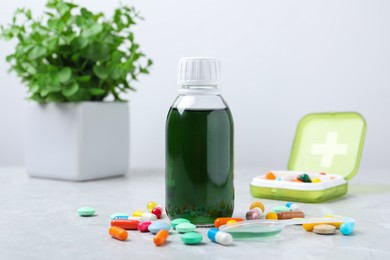 Photo of Bottle of syrup, dosing spoon and pills on white table. Cold medicine