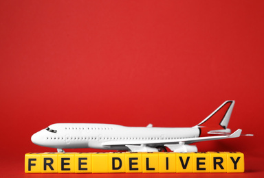 Photo of Toy plane and cubes with words FREE DELIVERY on red background, space for text. Logistics and wholesale concept