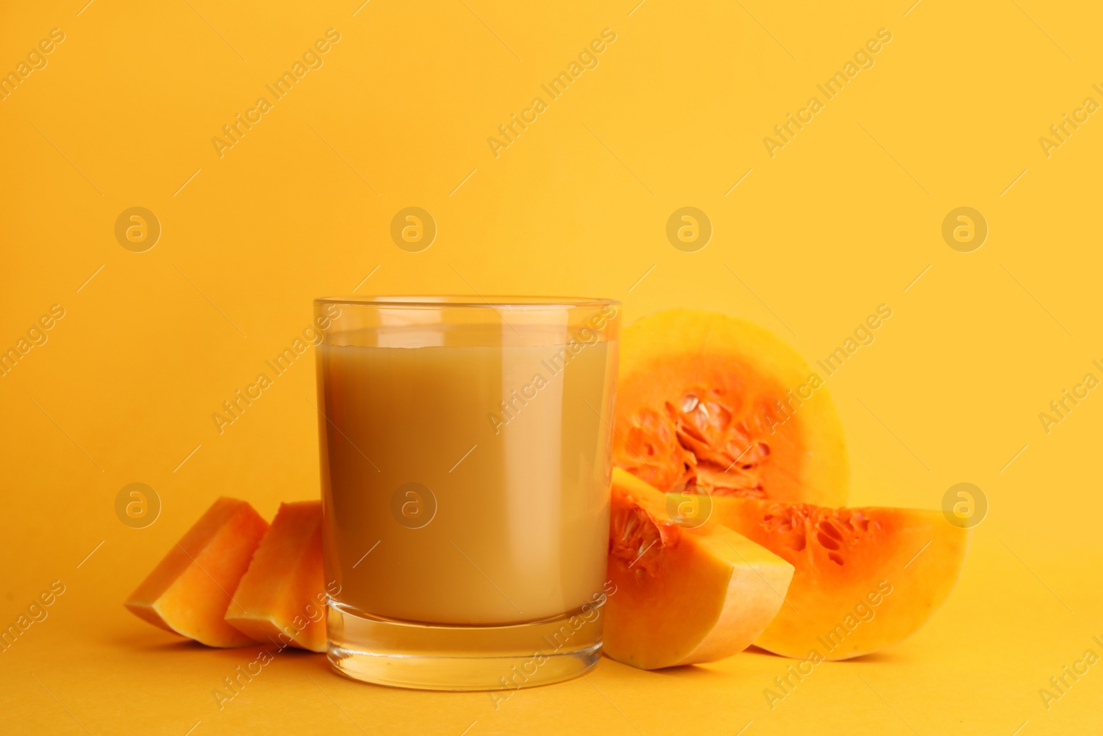 Photo of Tasty pumpkin juice in glass and cut pumpkin on orange background