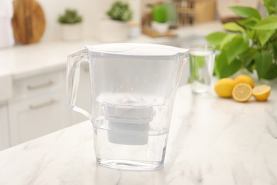 Photo of Water filter jug, glass and lemons on white marble table in kitchen