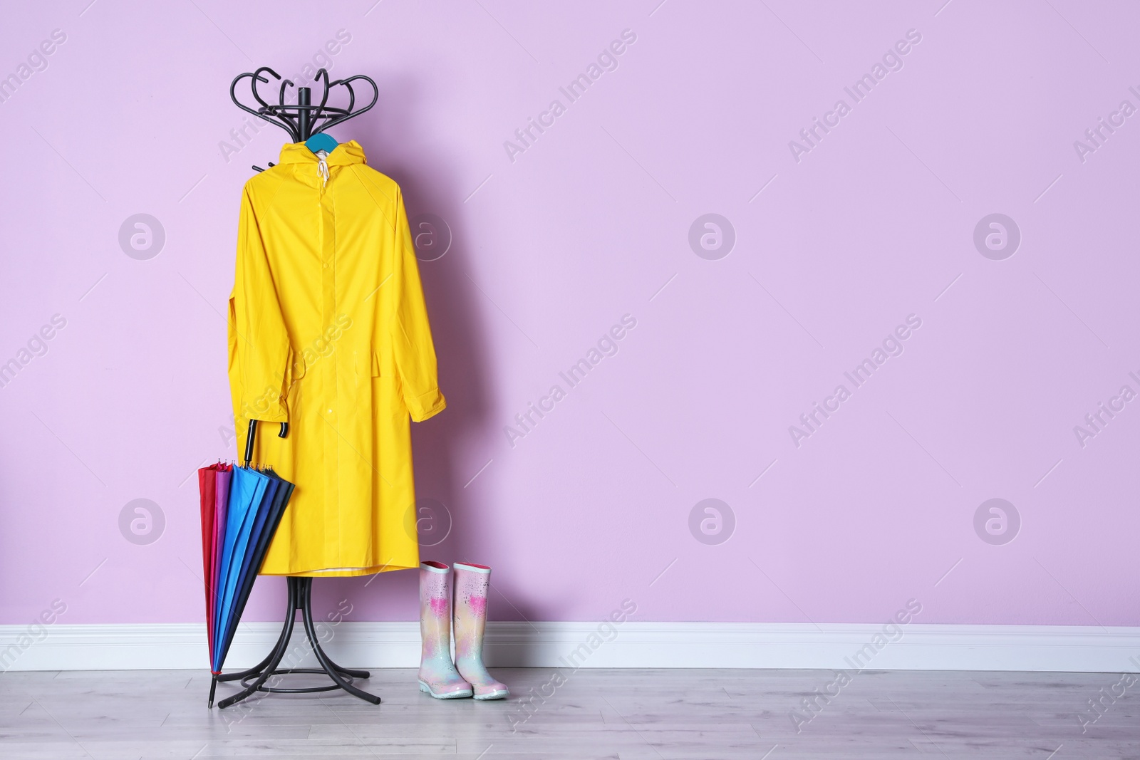 Photo of Umbrella, raincoat and gumboots near color wall with space for design