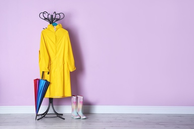 Photo of Umbrella, raincoat and gumboots near color wall with space for design