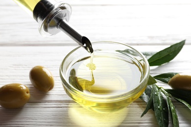 Photo of Pouring fresh olive oil into bowl on table