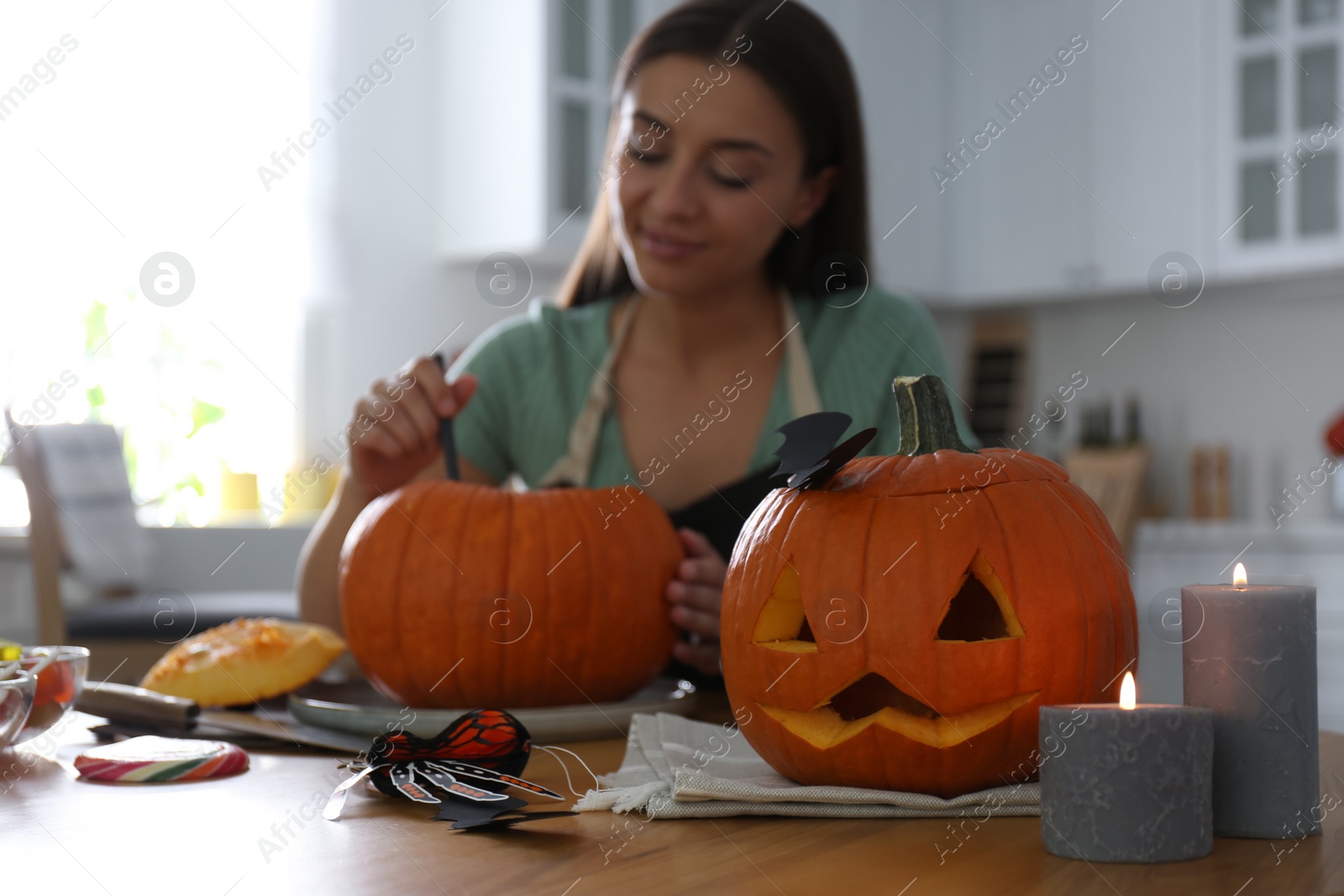 Photo of Woman making pumpkin jack o'lantern at table in kitchen. Halloween celebration