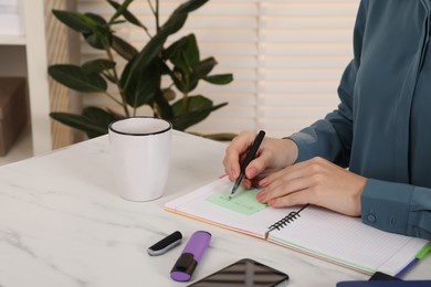 Woman writing on sticky note at white marble table indoors, closeup