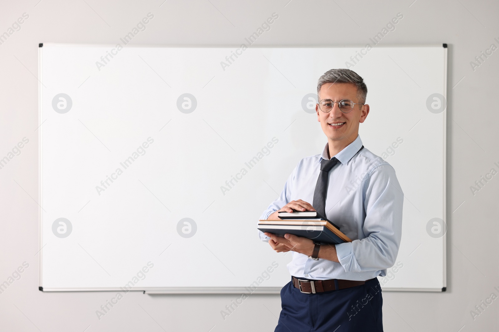 Photo of Teacher with notebooks near whiteboard in classroom