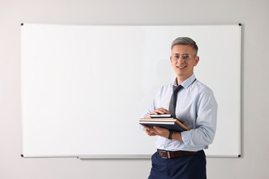Teacher with notebooks near whiteboard in classroom