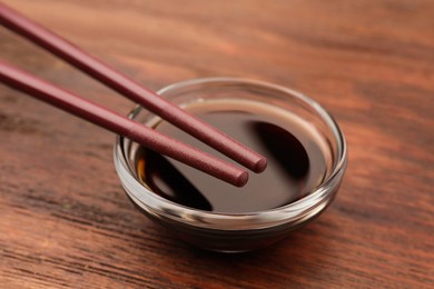 Photo of Bowl with soy sauce and chopsticks on wooden table, closeup