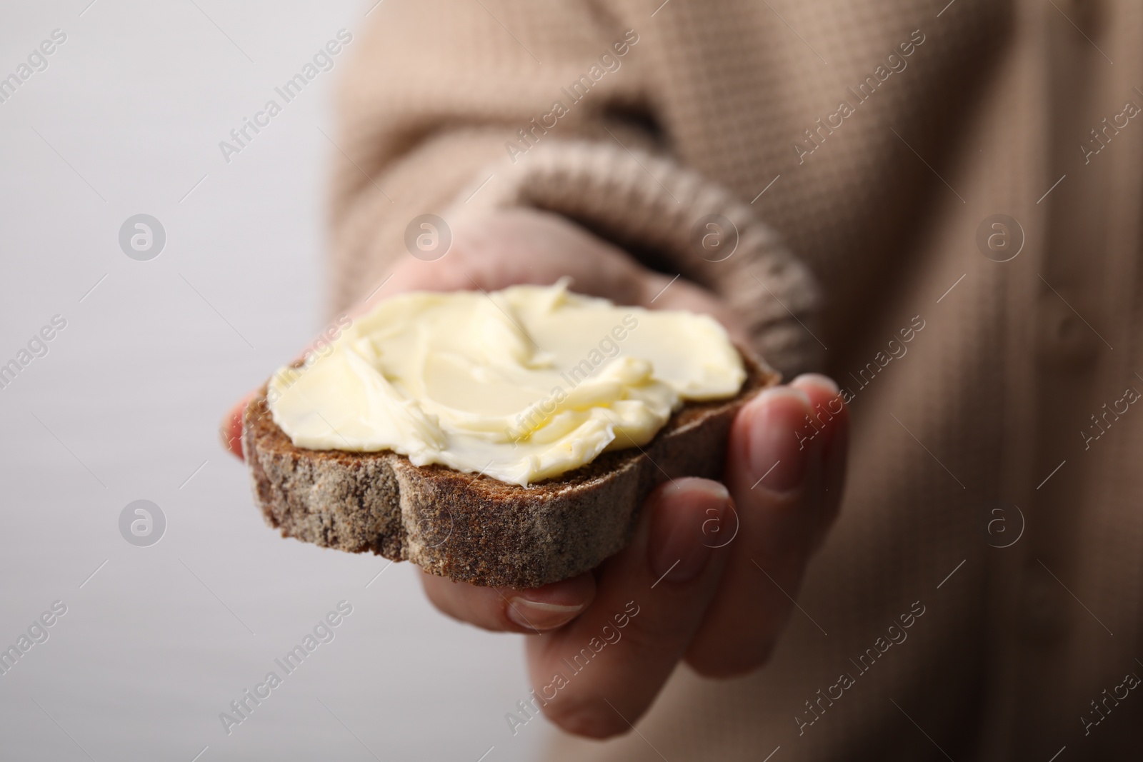 Photo of Woman holding slice of bread with butter on grey background, closeup