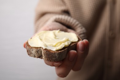 Woman holding slice of bread with butter on grey background, closeup