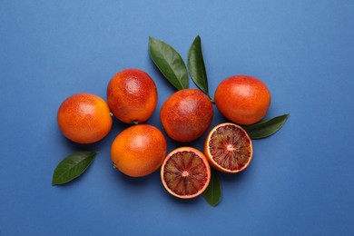 Photo of Many ripe sicilian oranges and leaves on blue background, flat lay