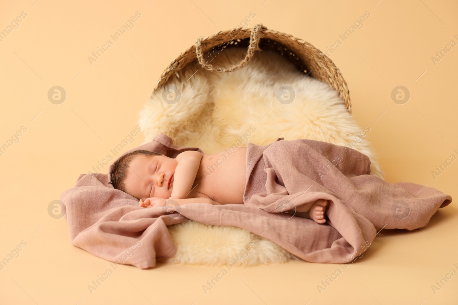 Photo of Adorable newborn baby sleeping on faux fur near overturned wicker basket against beige background