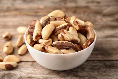 Photo of Bowl with tasty Brazil nuts on wooden background