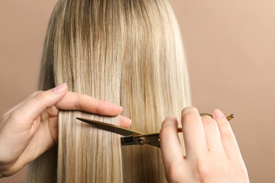 Photo of Hairdresser cutting client's hair with scissors on beige background, closeup