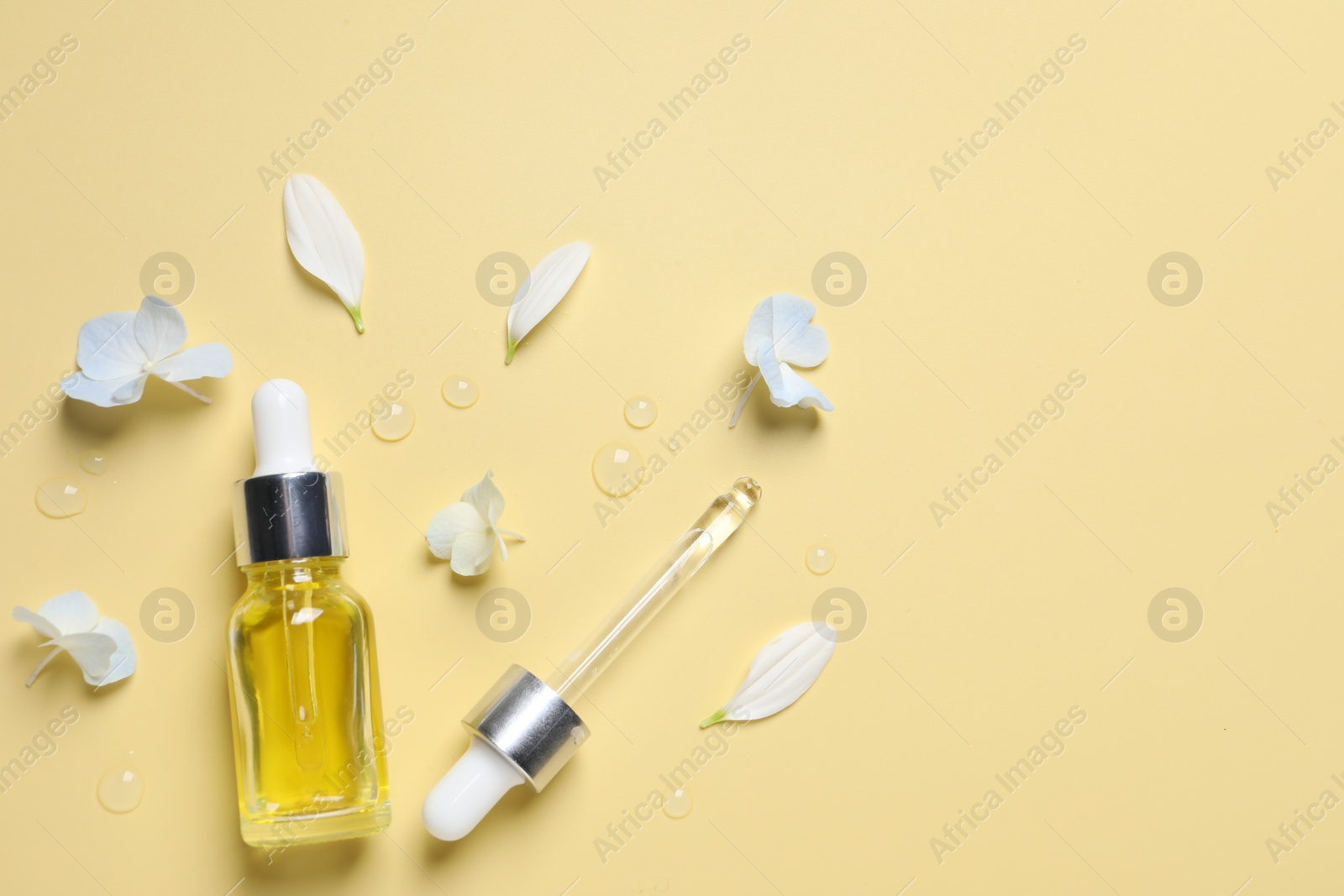 Photo of Bottle of cosmetic serum, pipette and beautiful flowers on pale yellow background, flat lay. Space for text