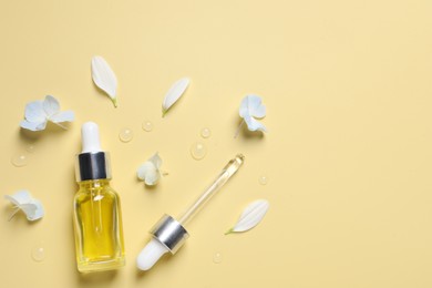 Bottle of cosmetic serum, pipette and beautiful flowers on pale yellow background, flat lay. Space for text
