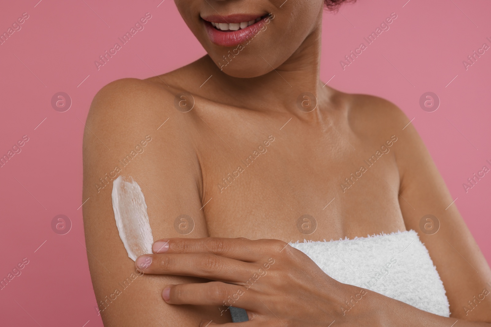 Photo of Young woman applying body cream onto arm on pink background, closeup