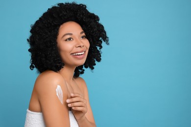 Photo of Young woman applying body cream onto shoulder on light blue background. Space for text