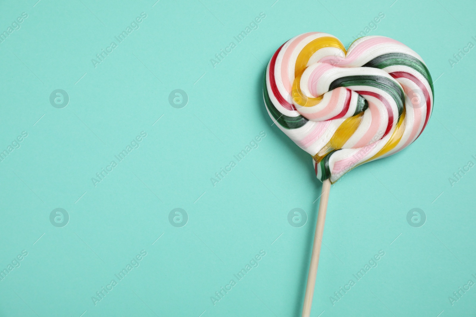 Photo of Stick with heart shaped lollipop on turquoise background, top view. Space for text