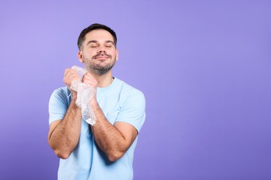 Happy man with bubble wrap on purple background. Space for text