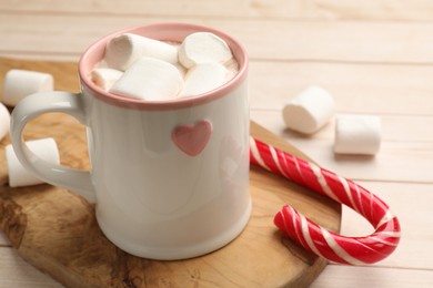 Photo of Tasty hot chocolate with marshmallows and candy cane on light wooden table, closeup