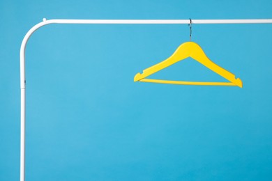 Photo of Yellow clothes hanger on metal rack against light blue background