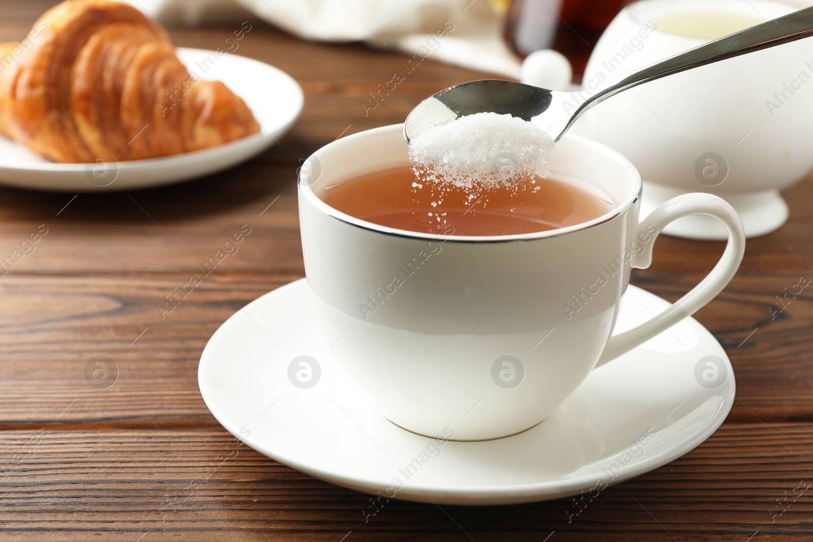 Photo of Adding sugar into cup of tea at wooden table, closeup