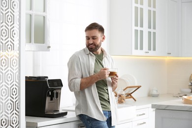 Young man enjoying fresh aromatic coffee near modern machine in kitchen