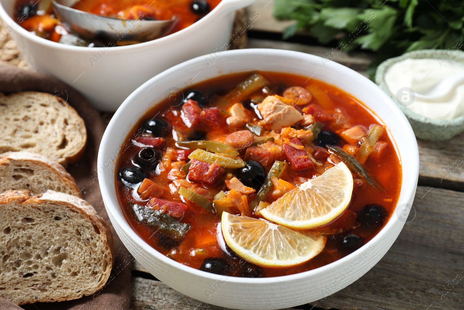 Photo of Meat solyanka soup with sausages, olives and vegetables served on wooden table, closeup