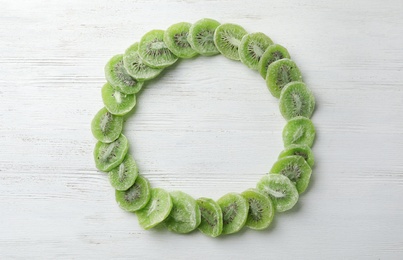 Photo of Frame made of kiwi on wooden background, top view with space for text. Dried fruit as healthy food