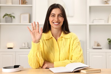 Photo of Happy woman waving hello at table indoors