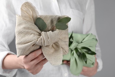 Photo of Furoshiki technique. Woman holding gifts packed in fabrics and decorated with green branches, closeup