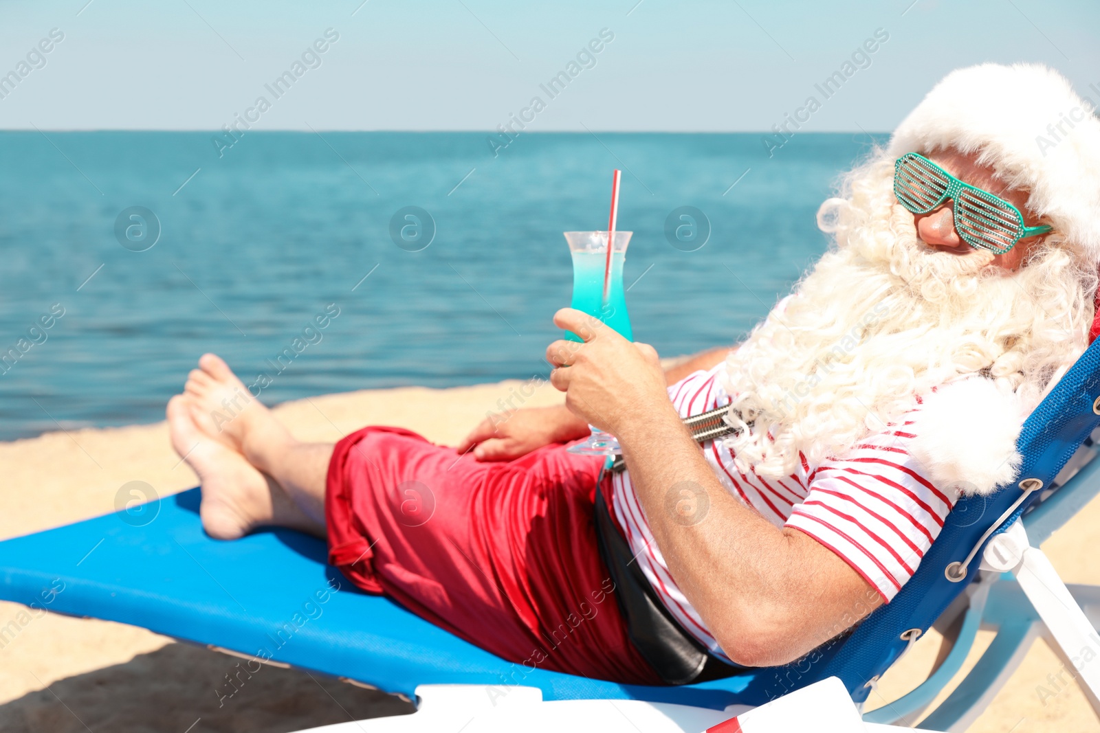 Photo of Authentic Santa Claus with cocktail resting on lounge chair at resort