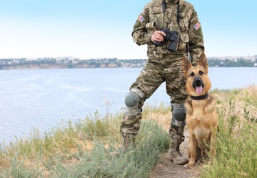 Man in military uniform with German shepherd dog near river